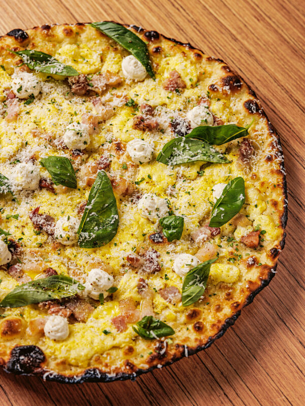 Pizza topped with cheese, spinach, and small dollops of cream, on a wooden surface.