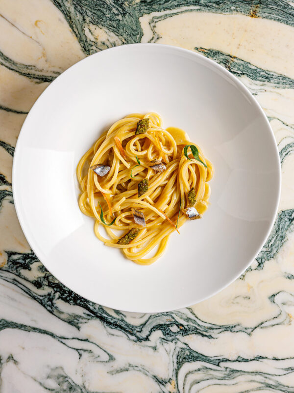 Linguine pasta with zucchini and herbs served in a white bowl on a marbled green and cream surface.