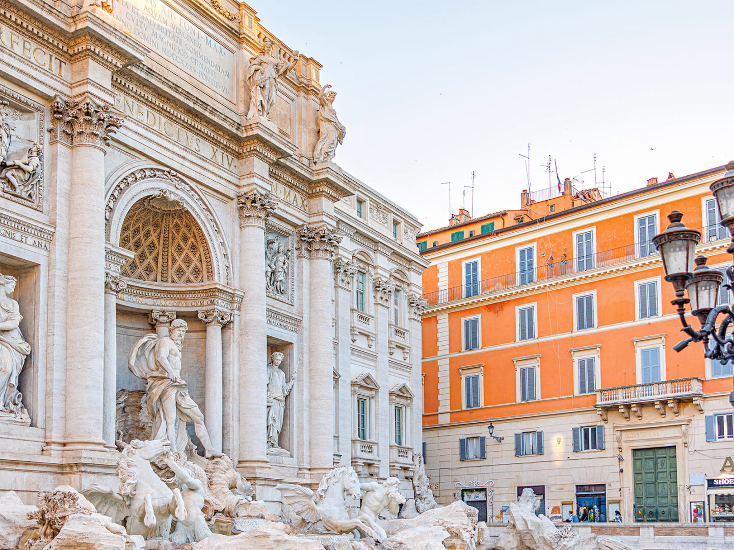 Trevi Fountain with intricate sculptures, surrounded by historic buildings in Rome, under a clear sky.