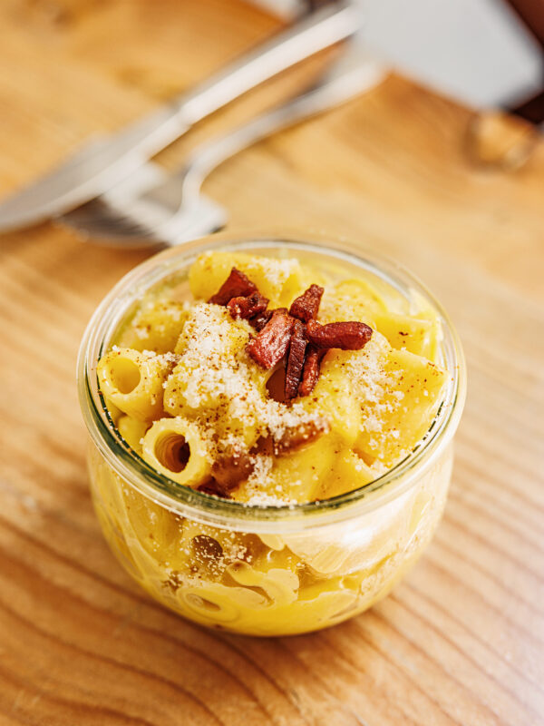 Creamy pasta with bacon and cheese served in a glass jar, placed on a wooden table.