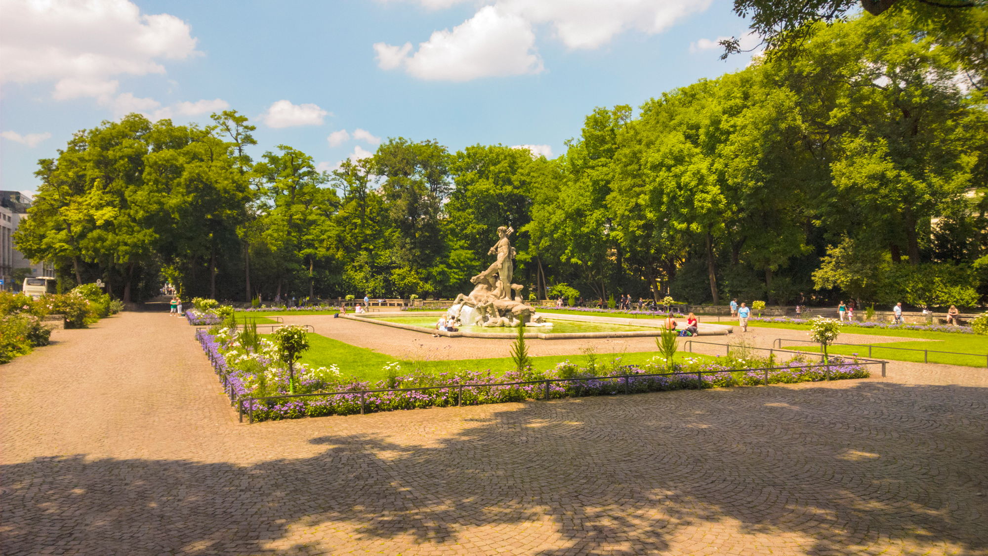 Botanical garden in Munich featuring a central fountain, surrounded by greenery and visitors on a sunny day.