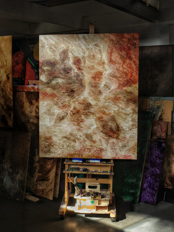 Abstract artwork displayed on an easel in an artist's studio, surrounded by various textured canvases.