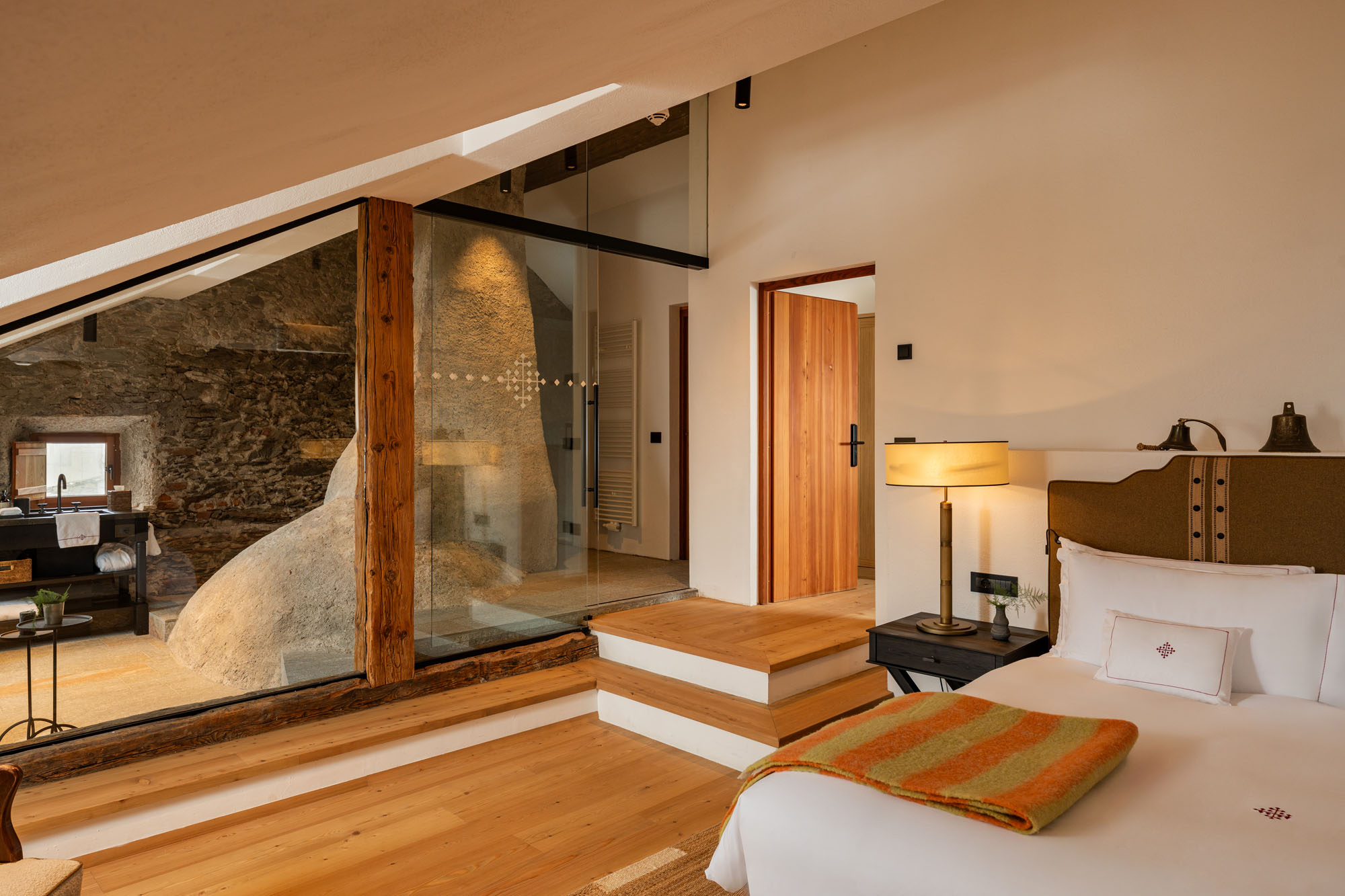 Modern chalet interior at Castel Badia, featuring a cozy bedroom, wooden floors, and a glass-walled sitting area.