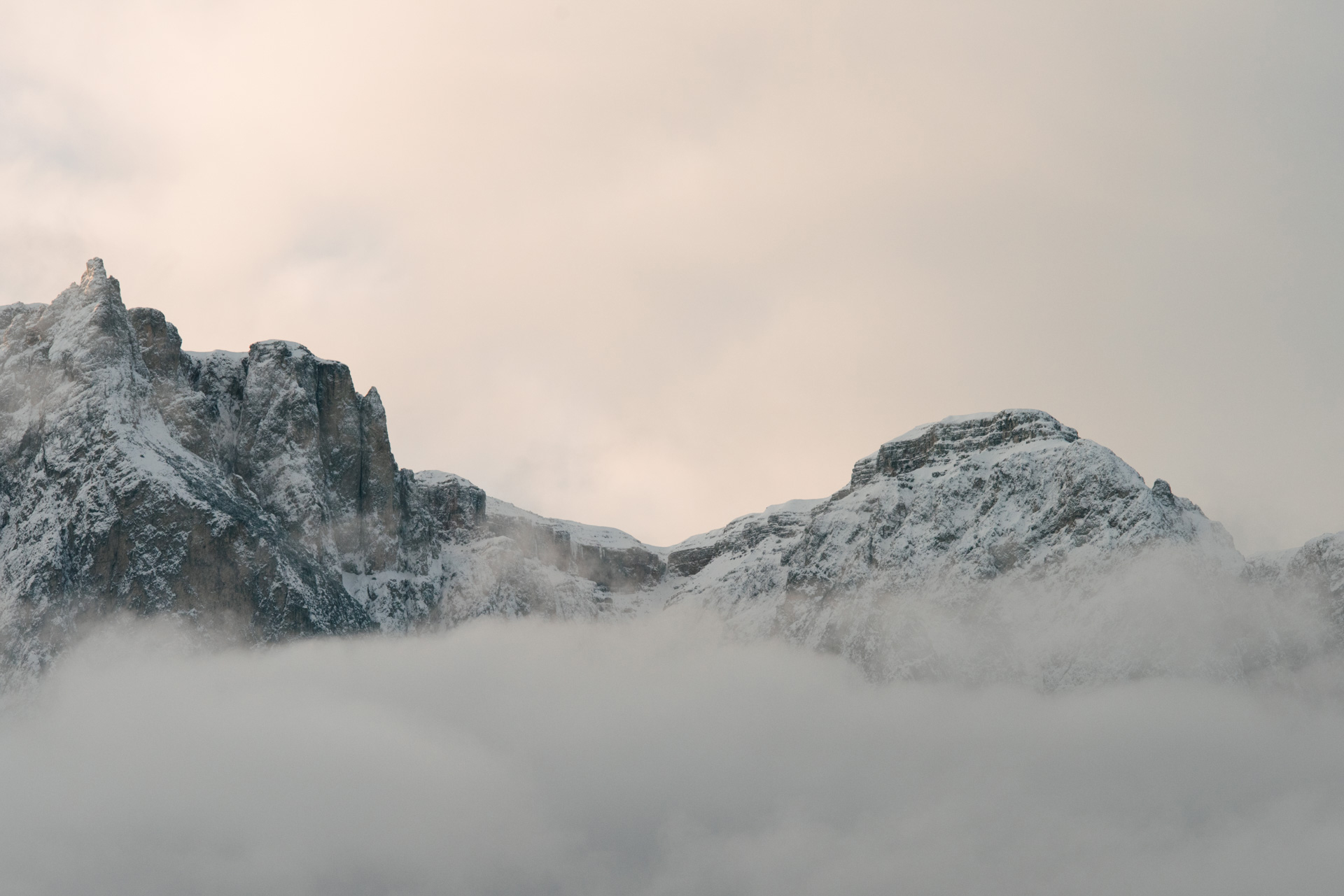 Snow-capped mountains partially obscured by clouds under a soft, cloudy sky.