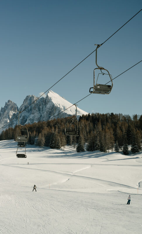 Ski lift chairs suspended over a snowy landscape with mountains and trees in the background.