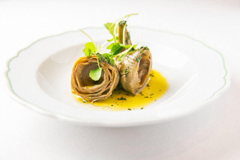 Carciofi alla Romana on a white plate, featuring rolled artichokes drizzled with olive oil and garnished with herbs.