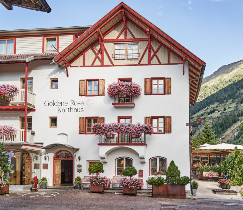 Charming hotel "Goldene Rose Karthaus" with flower-filled balconies, nestled in a mountainous landscape.
