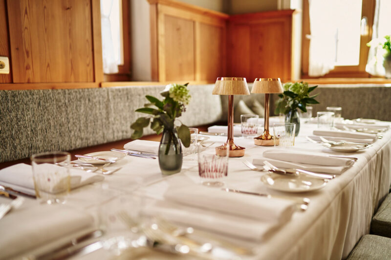 Elegant dining table set with white tablecloth, glassware, and decorative plants, in a warmly lit restaurant.