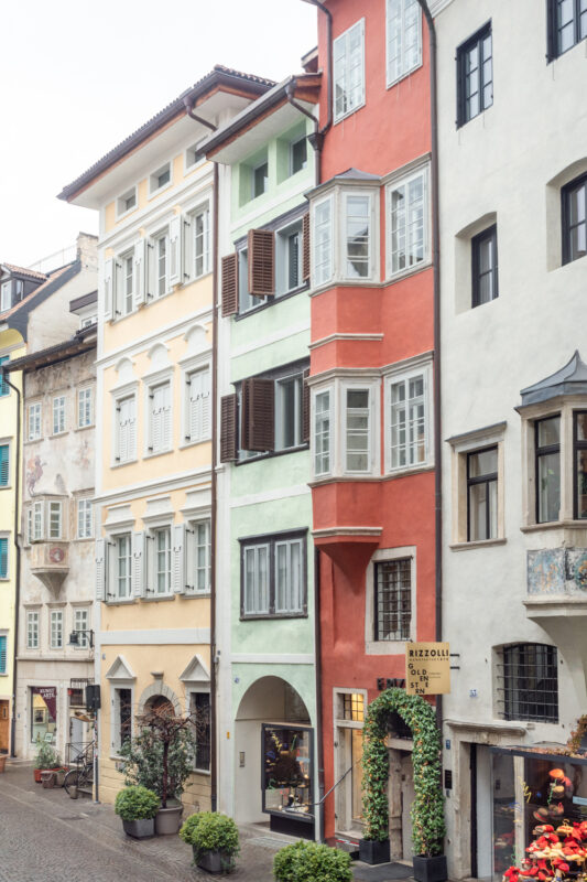 Colorful townhouse facades in a narrow street, featuring pastel yellow, green, and red buildings with shutters.