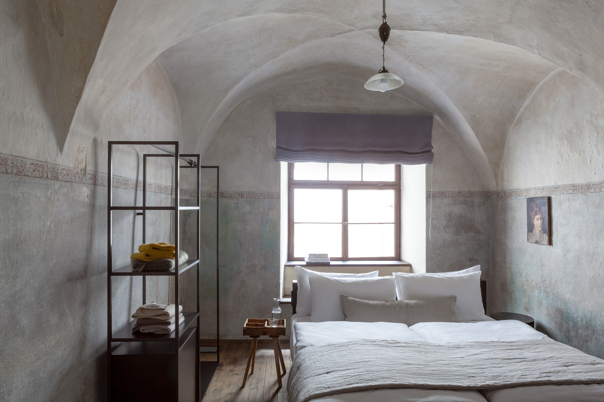 Cozy bedroom in Goldenstern Townhouse featuring a vaulted ceiling, large window, and minimalist decor with a shelf and art...