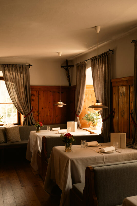 Cozy restaurant interior with wooden walls, tables set with white tablecloths, and flowers in vases, illuminated by pendan...
