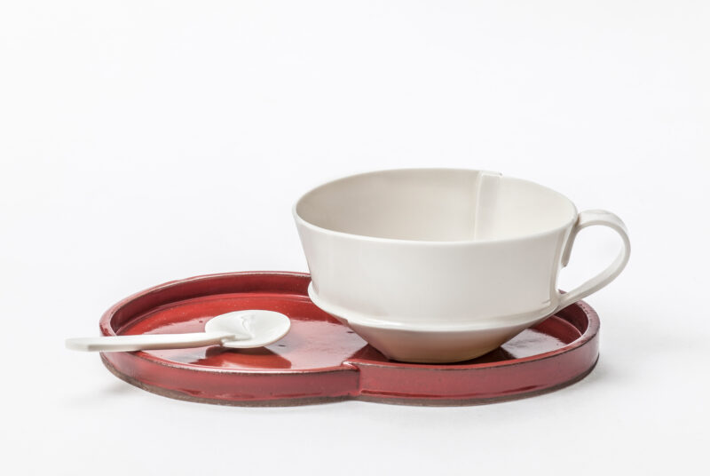 White cup on a red heart-shaped tray with a small spoon, against a white background.