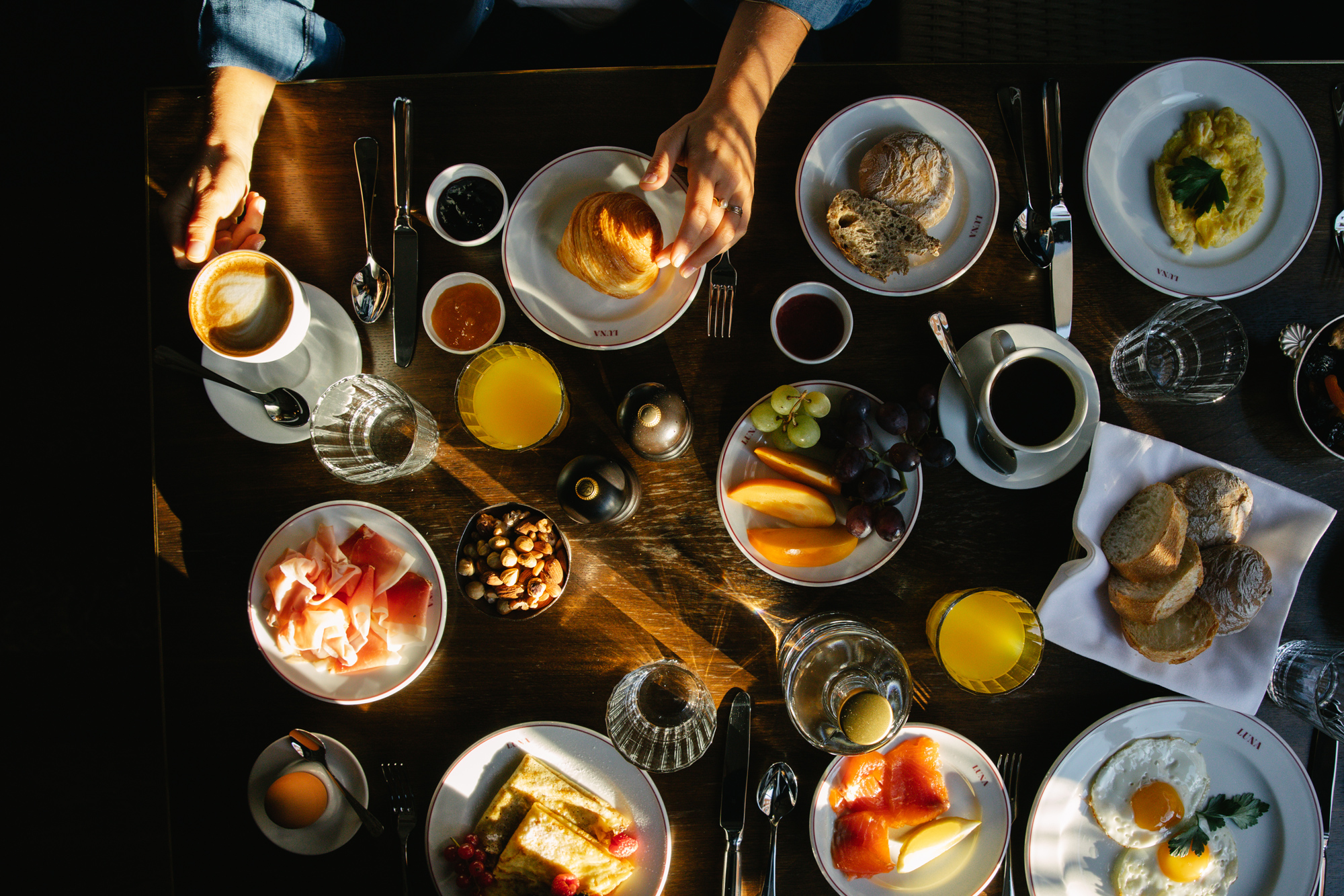 A top-down view of a breakfast spread featuring coffee, pastries, fruits, and various condiments on a wooden table.