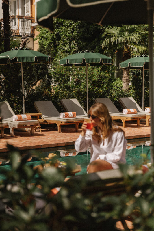 Woman in sunglasses sipping a drink by a pool, surrounded by lounge chairs and greenery at Parkhotel Mondschein.