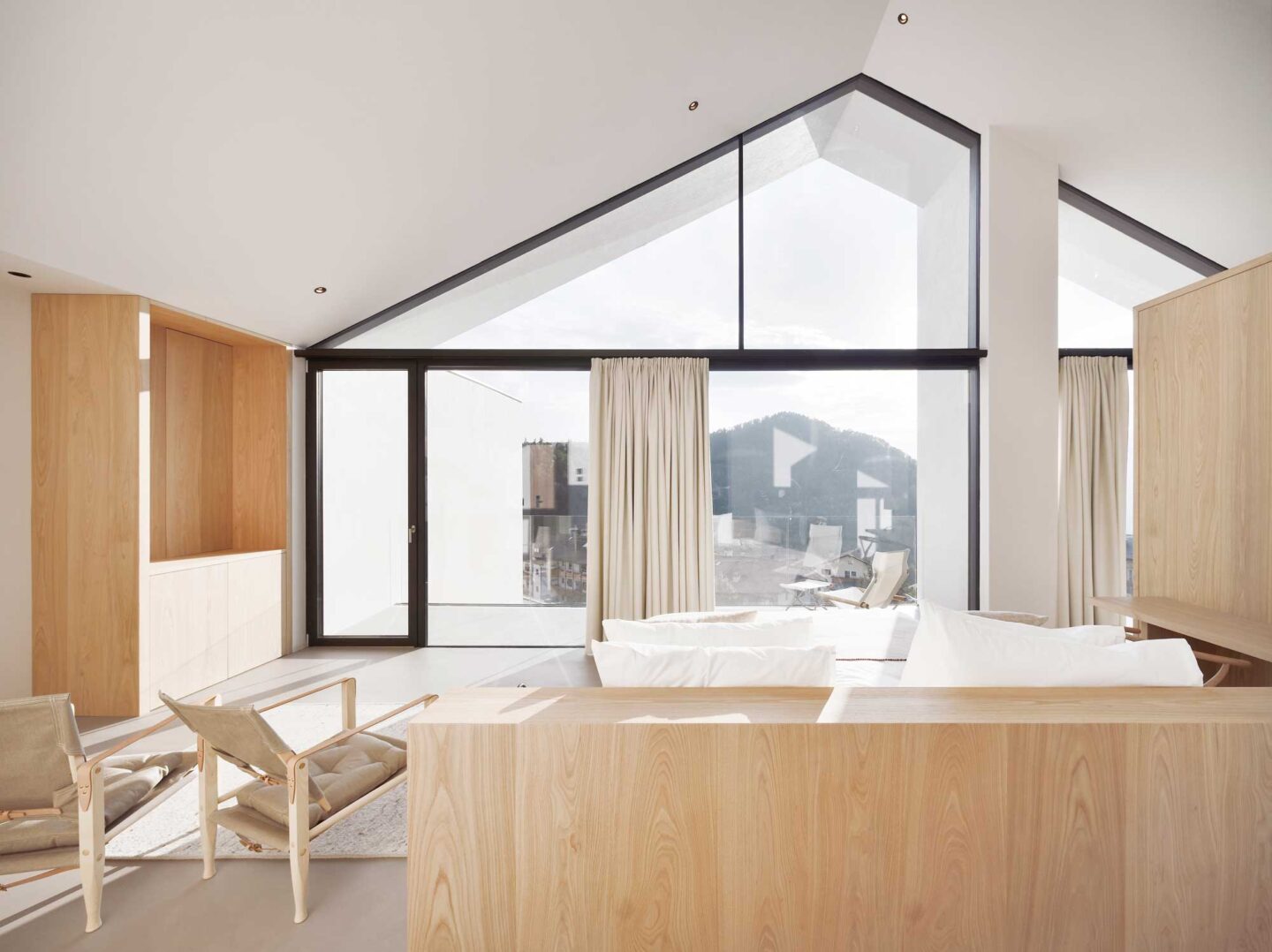 Modern loft suite with wooden furnishings, large windows, and a mountain view, featuring a minimalist design.