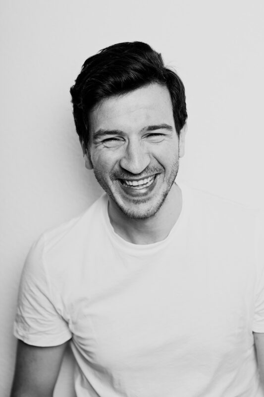 Smiling man in a white t-shirt against a light background, exuding a joyful expression.