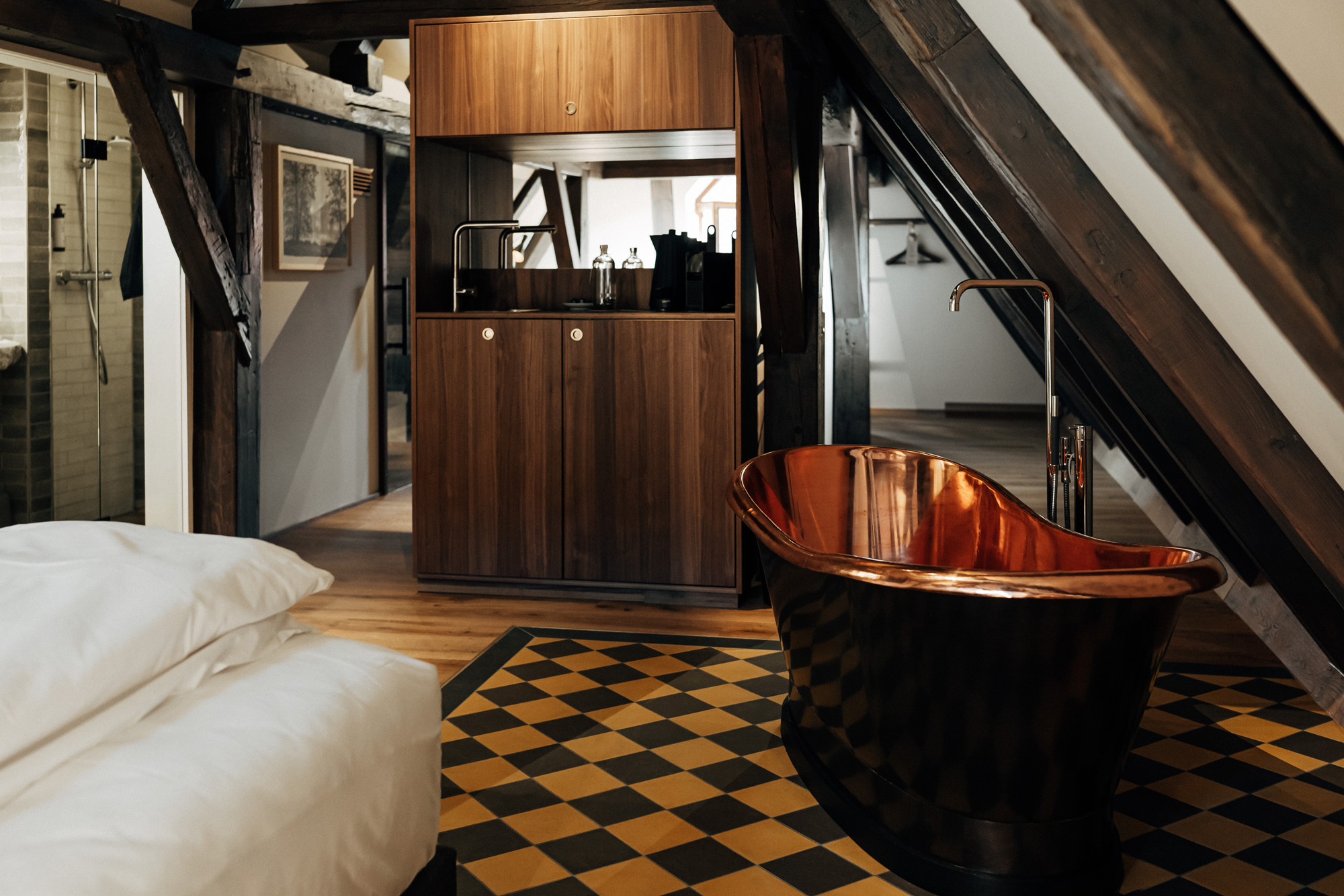 Stylish attic room featuring a copper bathtub, wooden cabinetry, and a checkered floor.