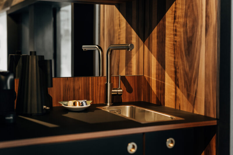Modern kitchen countertop featuring a sleek faucet, wooden paneling, and a small plate with pastries.