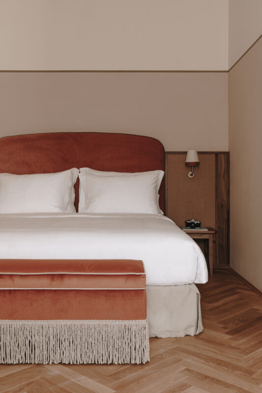 Elegant hotel room featuring a plush bed with white linens, a rust-colored headboard, and wooden accents.