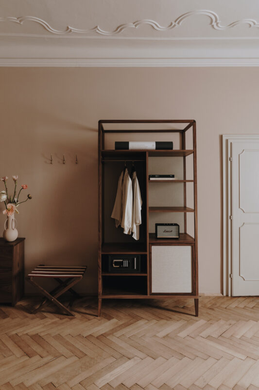 Modern wooden wardrobe with open shelves, a hanging space, and a closed section, set in a light-colored room with herringb...