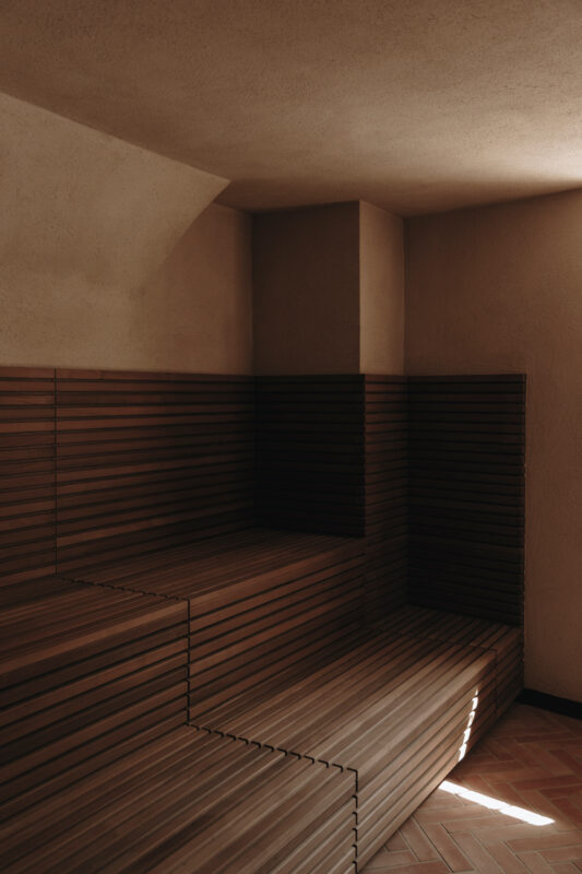 Wooden seating in a minimalist sauna with soft lighting and textured walls at Parkhotel Mondschein.