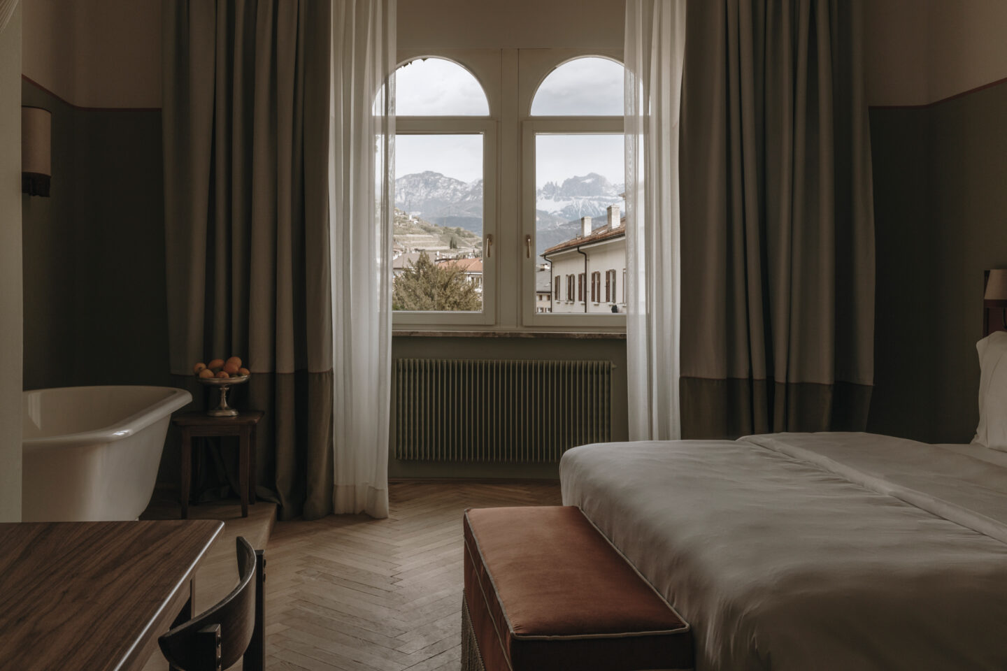 Cozy hotel room with a bed, wooden furniture, and a large window revealing mountain views.