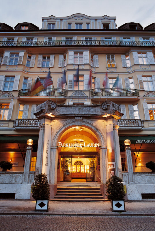 Elegant entrance of Parkhotel Laurin, featuring a grand archway, illuminated signage, and flags displayed above.