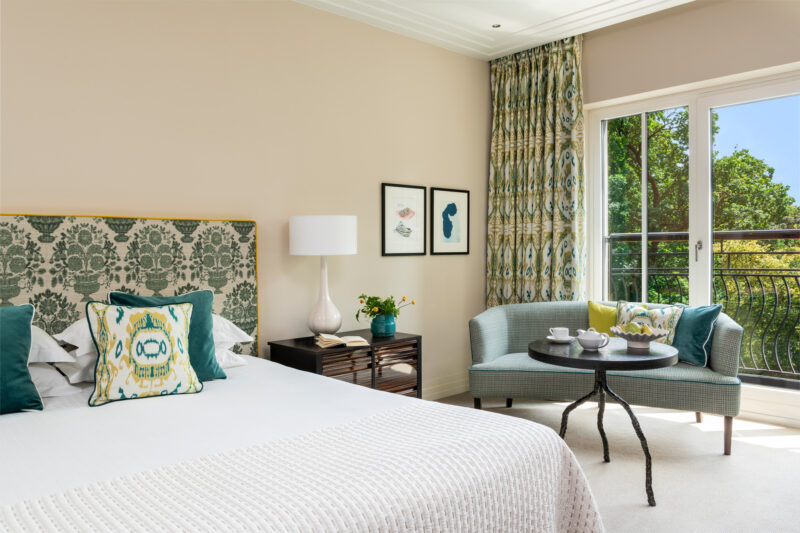 Deluxe Park View Room at The Charles Hotel featuring a bed, seating area, and balcony with greenery outside.