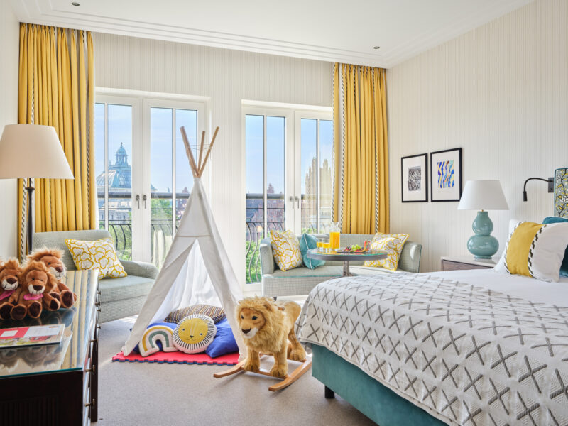 Bright family room at The Charles Hotel featuring a bed, colorful decor, a teepee, and a view of the city skyline.