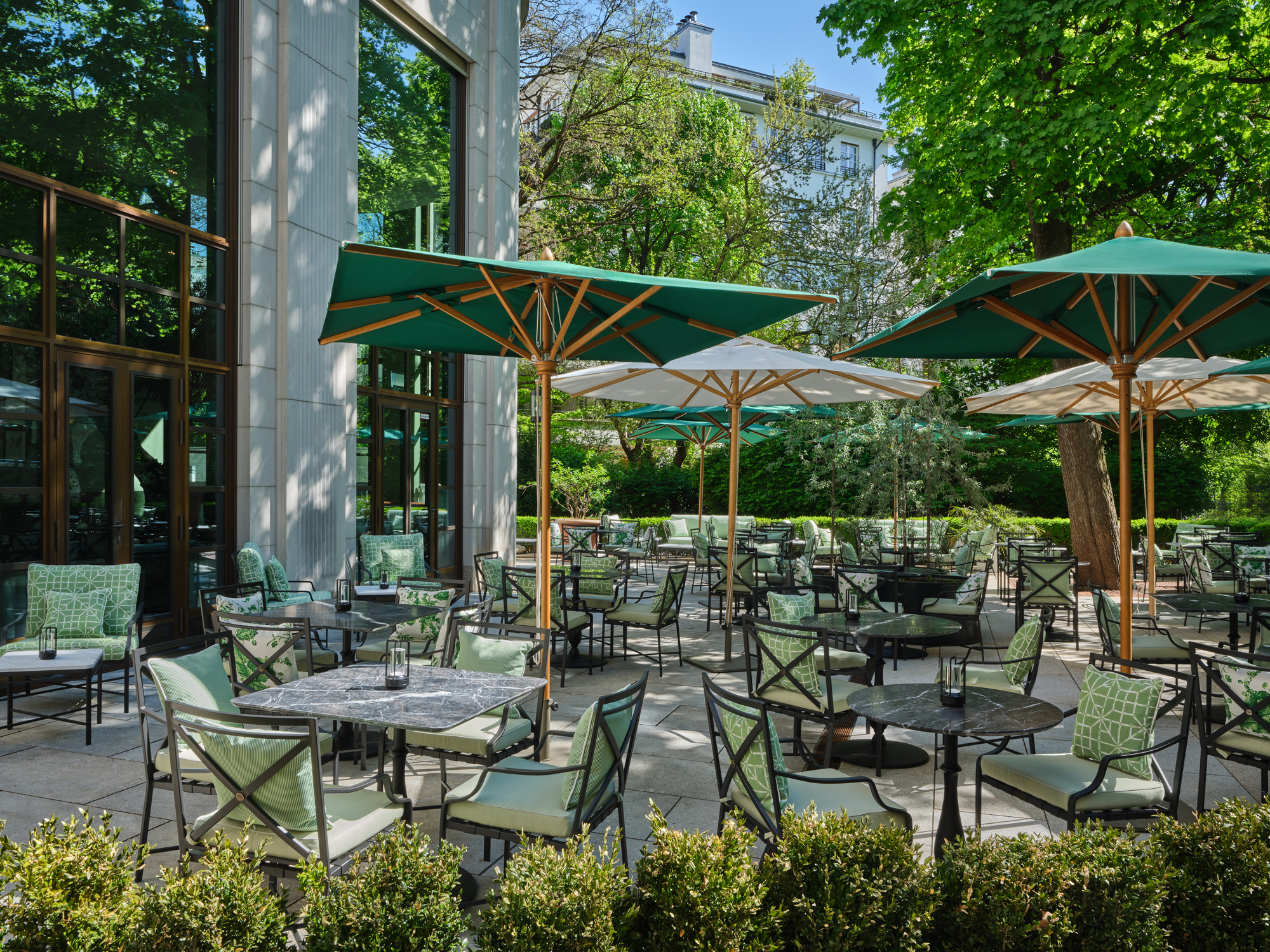 Outdoor dining area at The Charles Hotel featuring green umbrellas, tables, and chairs surrounded by lush greenery.