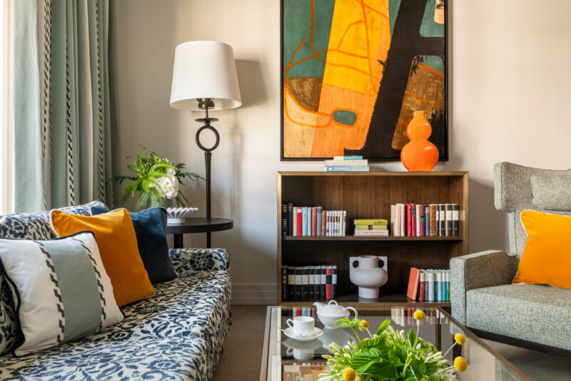 Stylish junior suite with a patterned sofa, vibrant orange accents, a modern art piece, and a cozy reading nook.