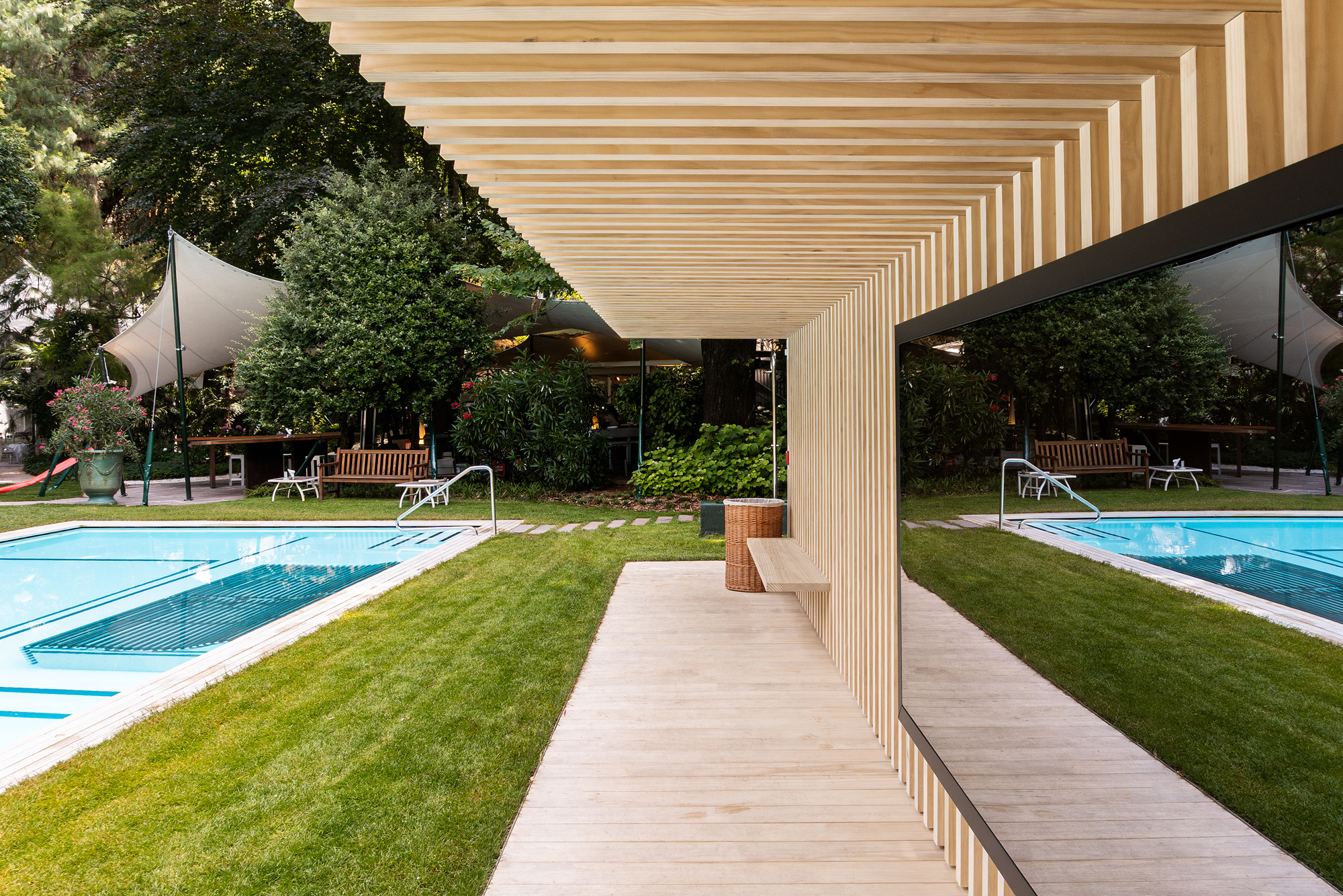 Wooden structure framing a view of a pool area with loungers, surrounded by greenery at Parkhotel Laurin.