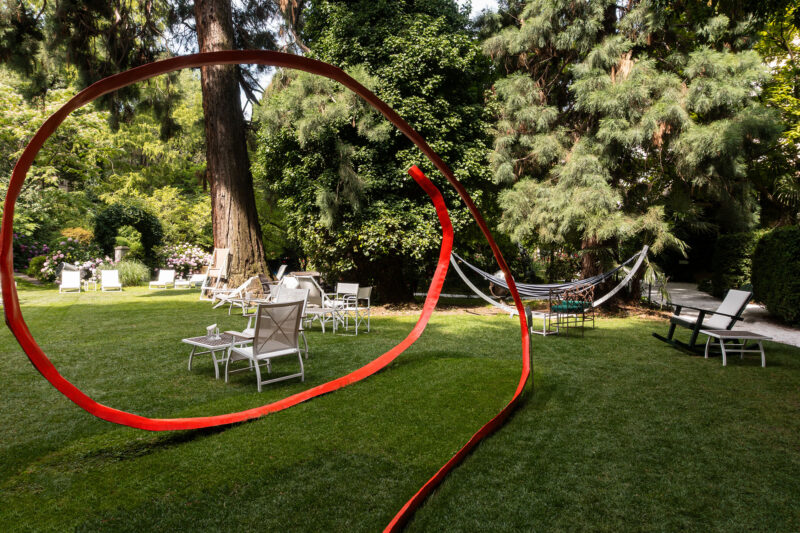 Red ribbon curves through a garden with white lounge chairs, a hammock, and lush greenery at Parkhotel Laurin.