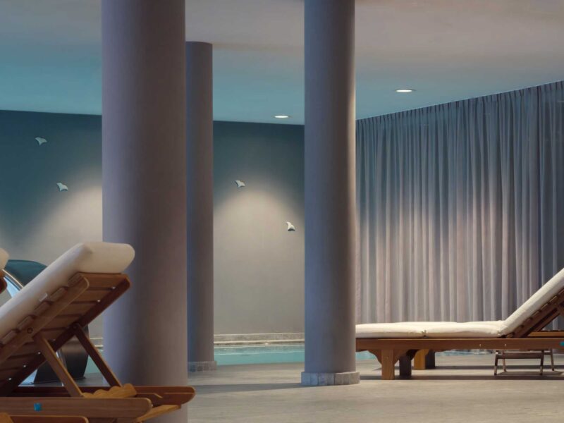 Indoor spa area featuring lounge chairs, columns, and soft lighting, with curtains and decorative wall elements.