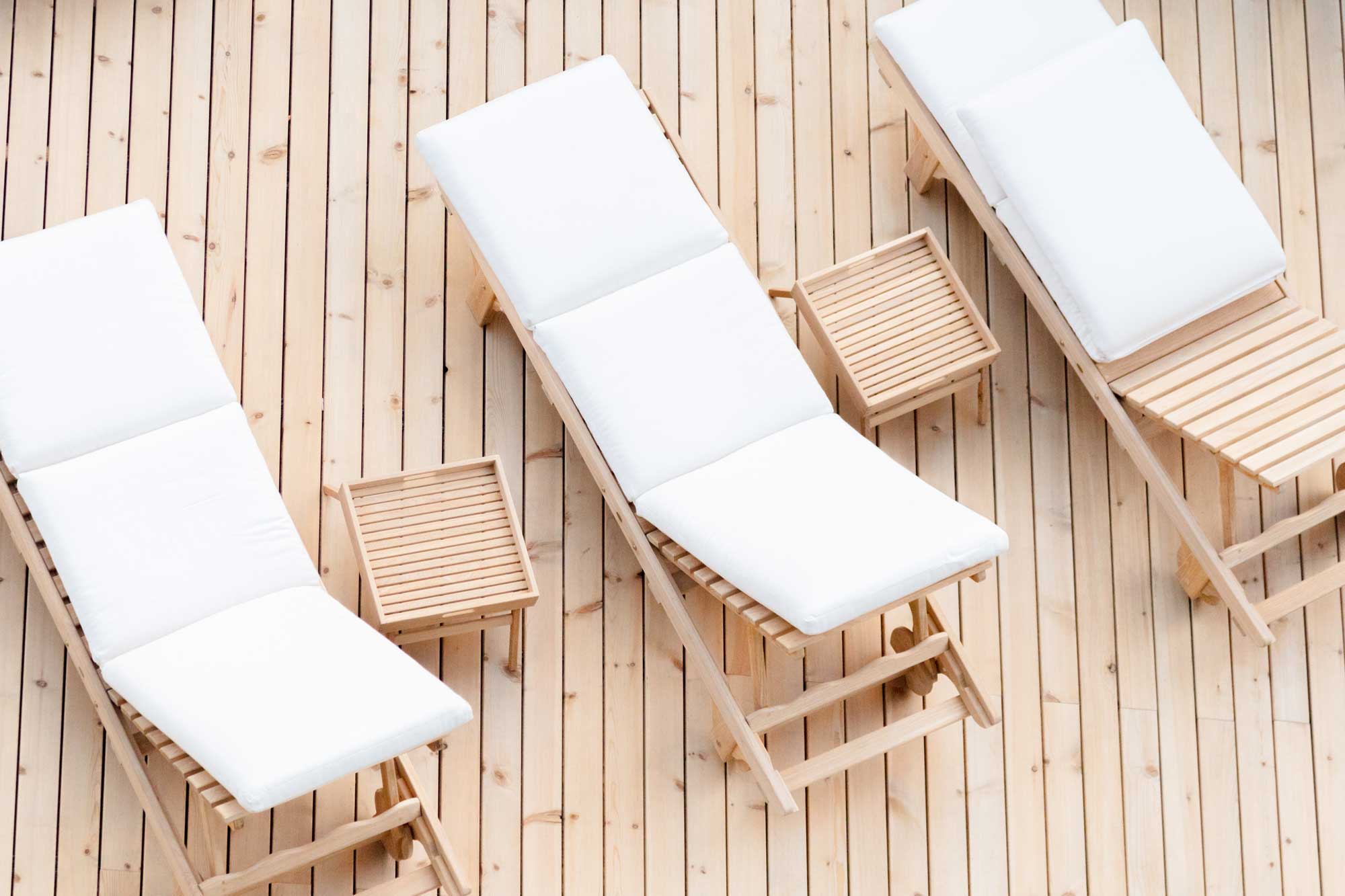 Three white lounge chairs with wooden frames and a small side table on a wooden deck.