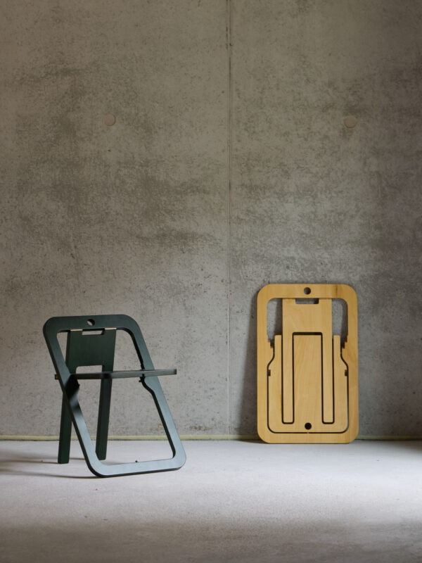 Two minimalist folding chairs, one green and one light wood, positioned against a textured gray wall.