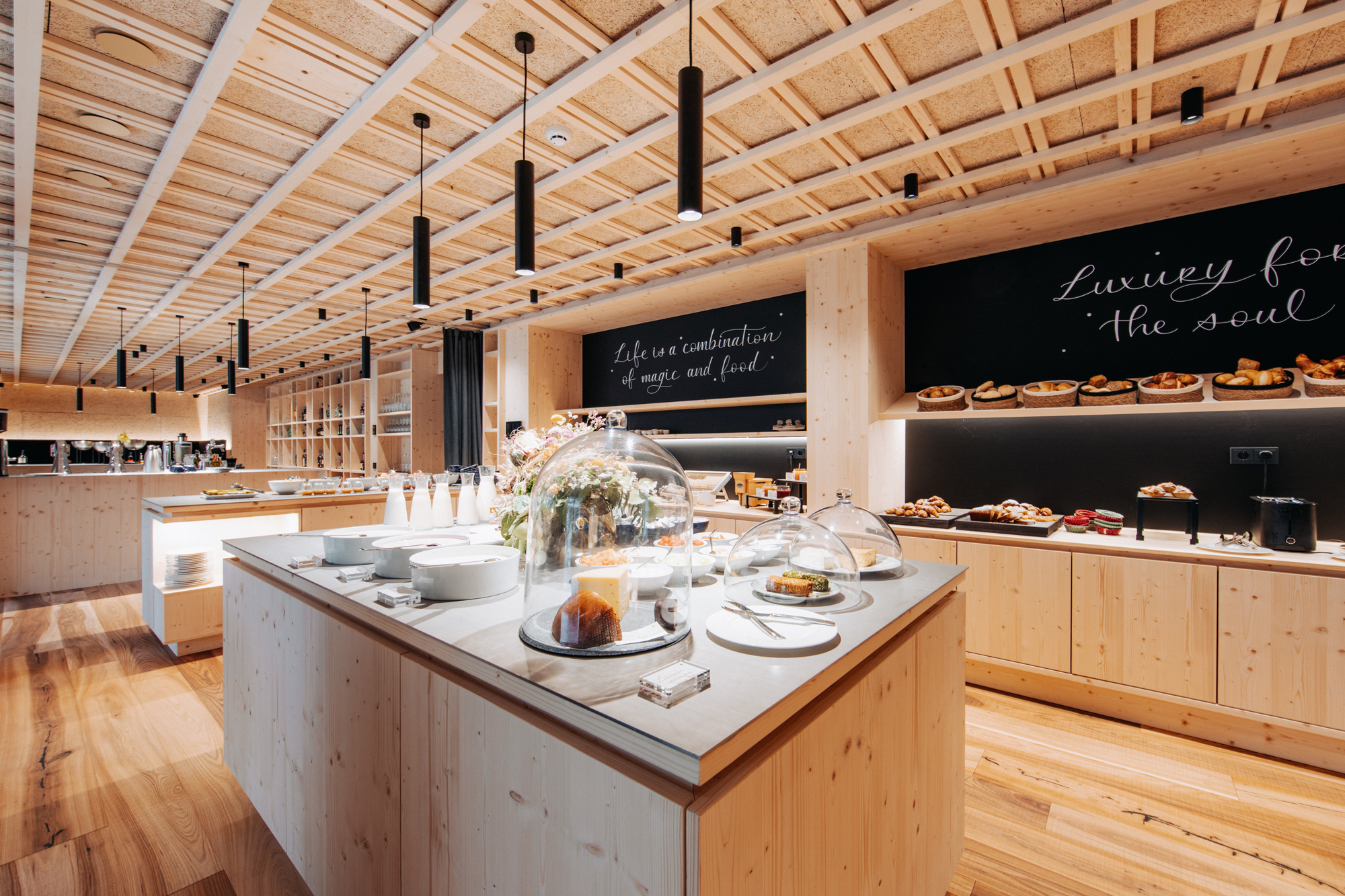 Modern interior of a gourmet market featuring wooden shelves, a display of pastries under glass domes, and chalkboard walls.