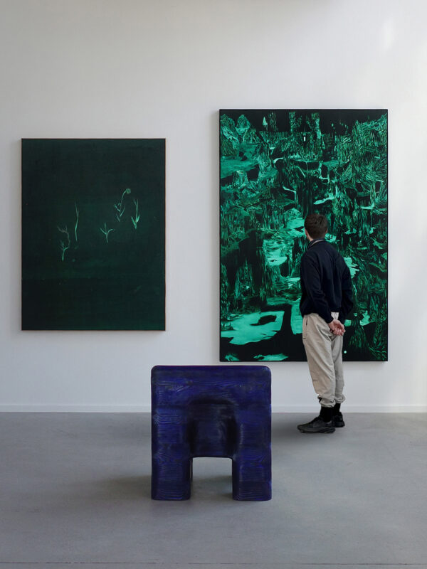 Visitor observing two abstract paintings in a gallery, with a blue sculpture in the foreground.