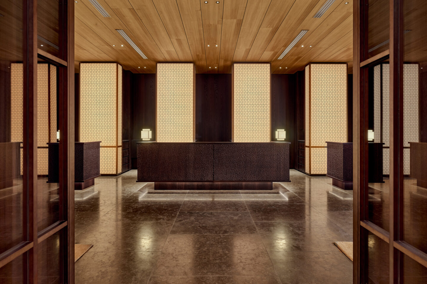 Modern hotel lobby with wooden ceiling, illuminated panel walls, and a sleek reception desk.