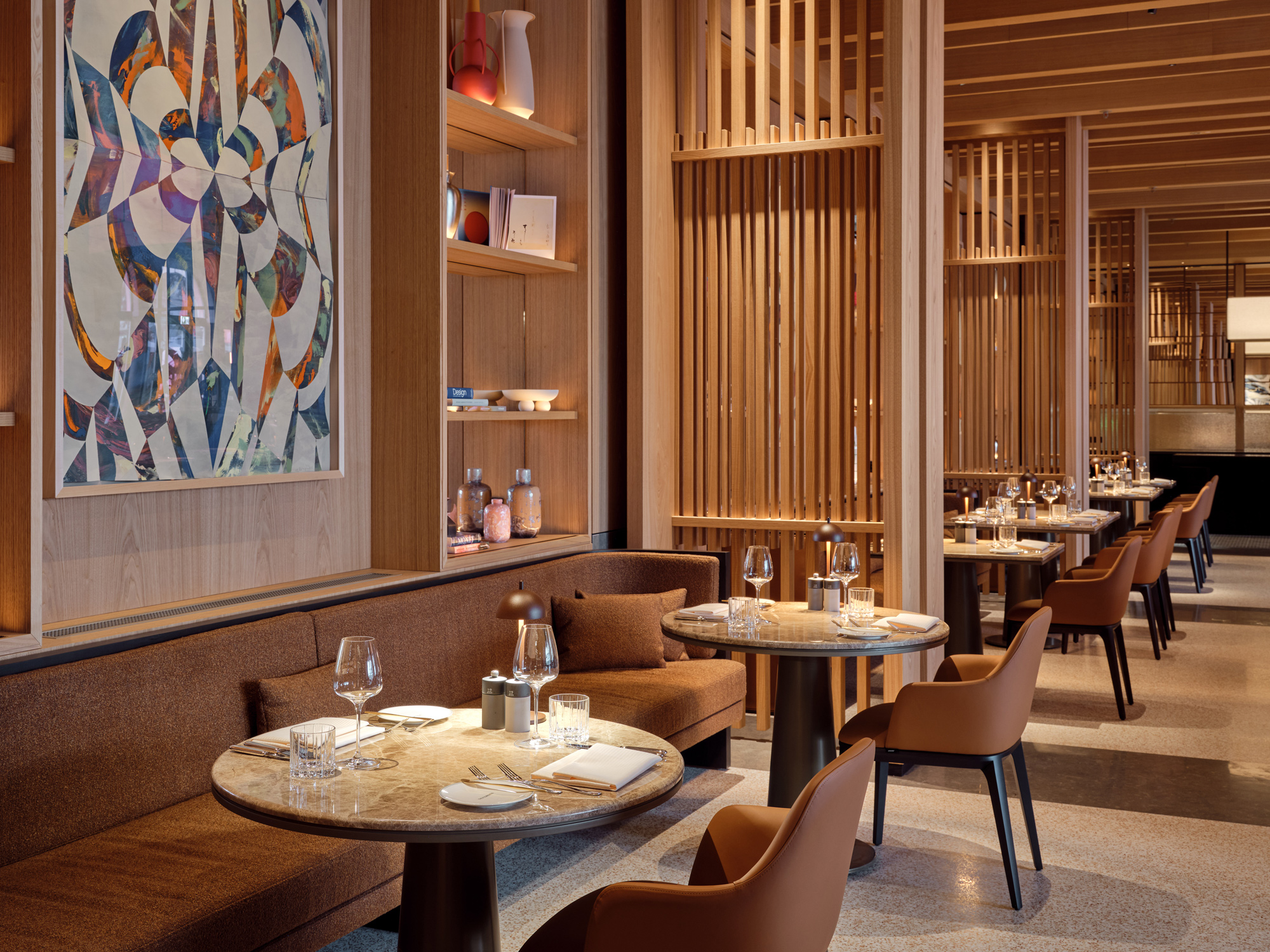Modern restaurant interior featuring wooden accents, circular tables, and colorful artwork on the wall.