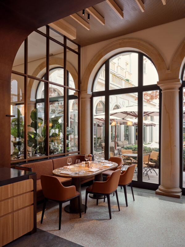 Elegant dining area with a round table set for four, surrounded by large windows and views of a garden.