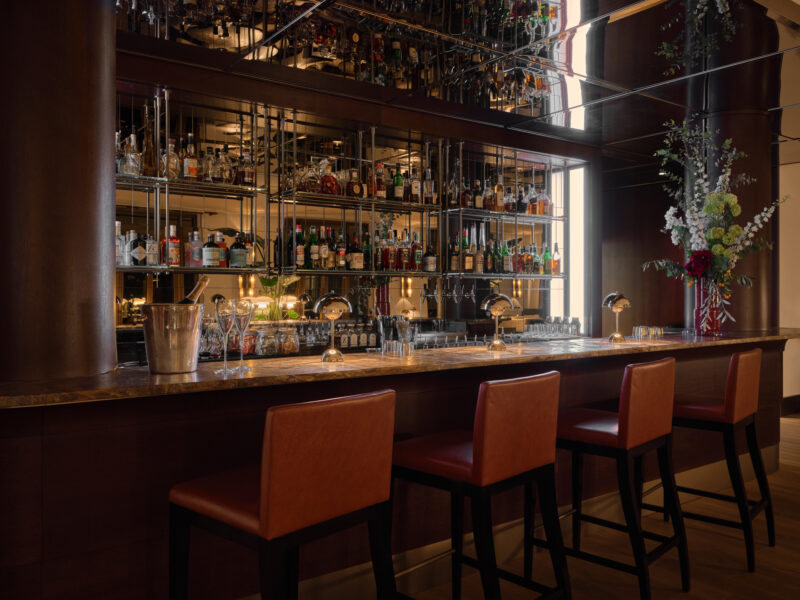 Elegant bar area at The Charles Hotel, featuring a mirrored backdrop, shelves of liquor, and stylish seating.