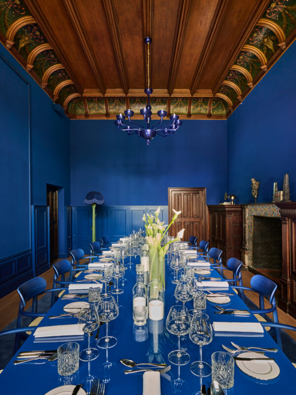 Elegant blue dining room featuring a long table set with glassware and floral centerpieces, ornate ceiling, and blue decor.