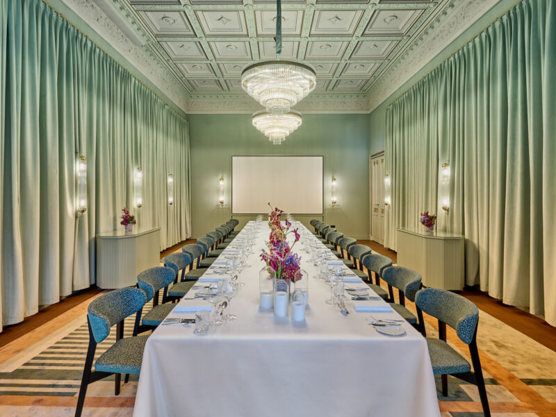 Elegant dining setup in a room with green walls, a long table adorned with flowers, and chandeliers overhead.