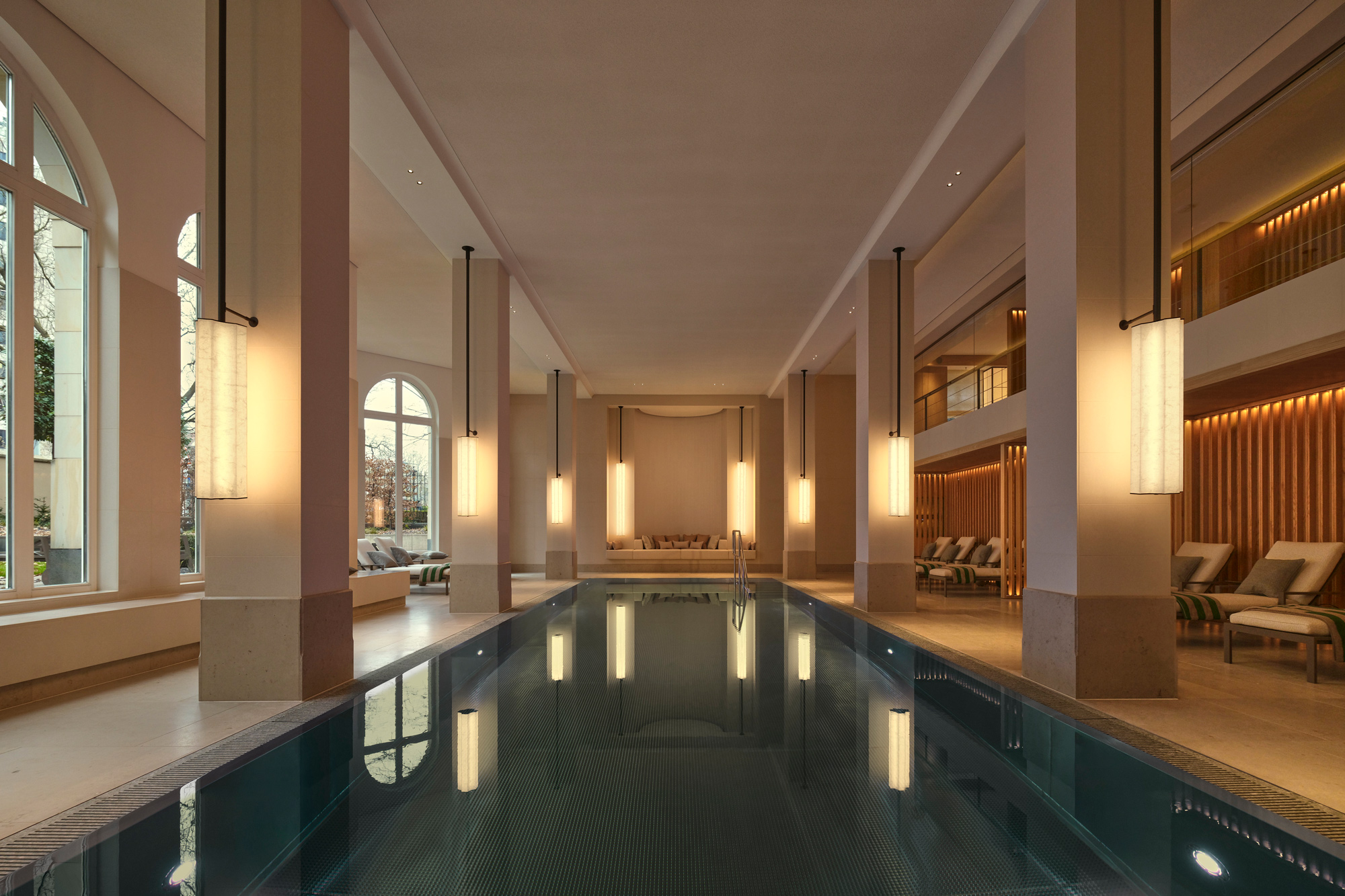 Indoor spa area featuring a serene pool, elegant lighting, and lounge chairs, with large windows letting in natural light.