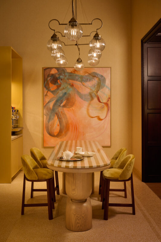 Modern kitchen dining area featuring a striped table, four yellow chairs, and an abstract painting on the wall.