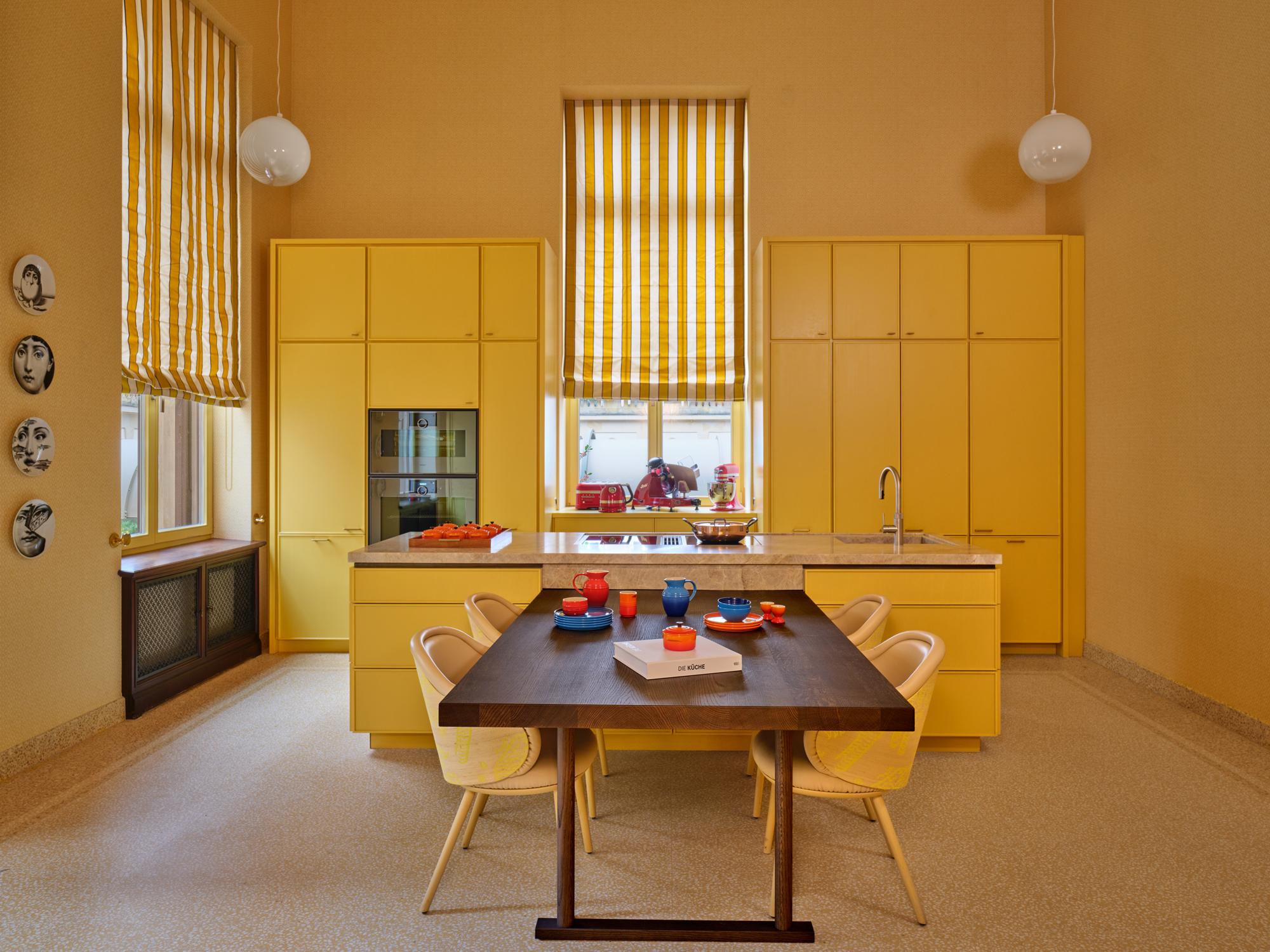 Bright yellow kitchen with striped curtains, a wooden table set with colorful dishes, and modern cabinetry.