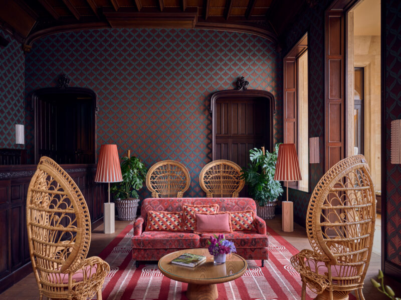 Elegant lobby of The Florentin featuring a pink sofa, rattan chairs, patterned wallpaper, and decorative plants.