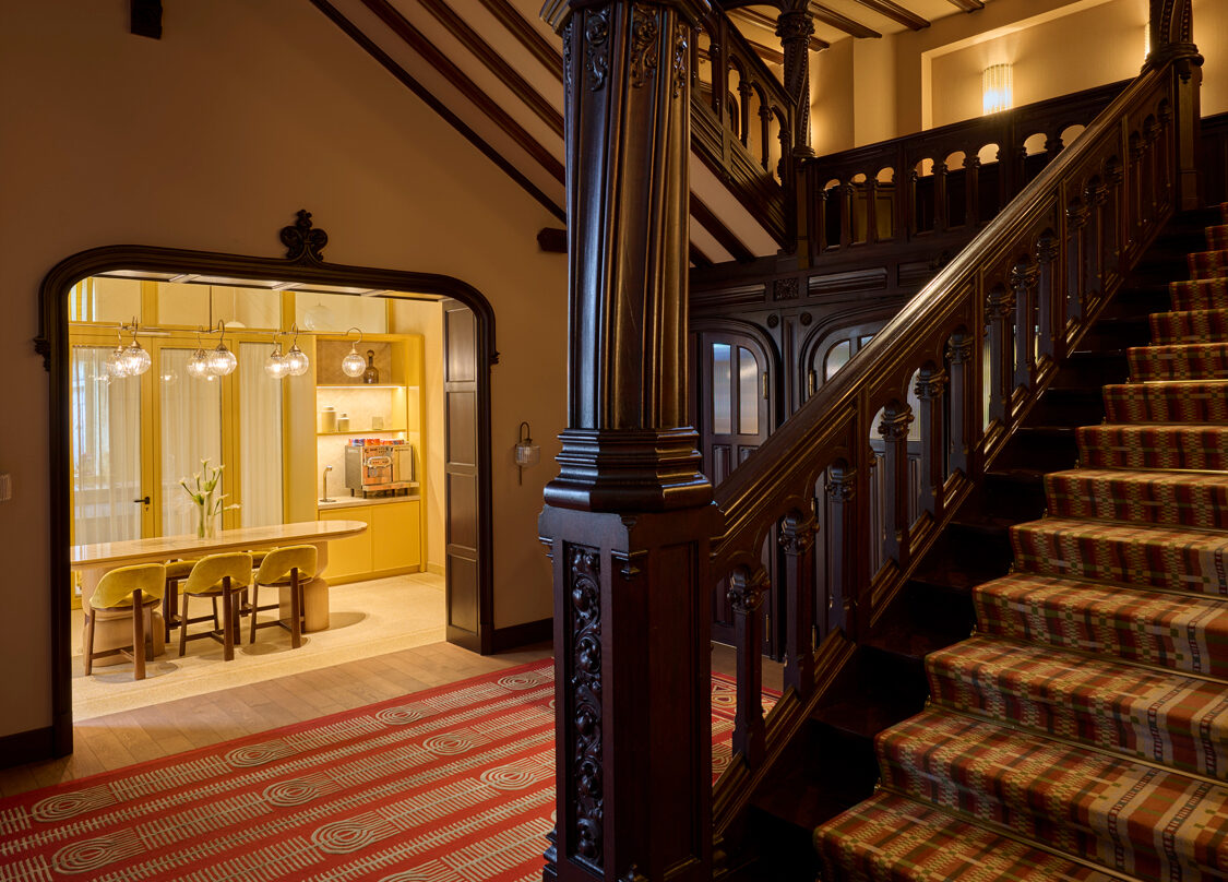 Elegant villa lobby featuring a grand staircase with ornate wooden details and a patterned carpet, leading to a bright din...