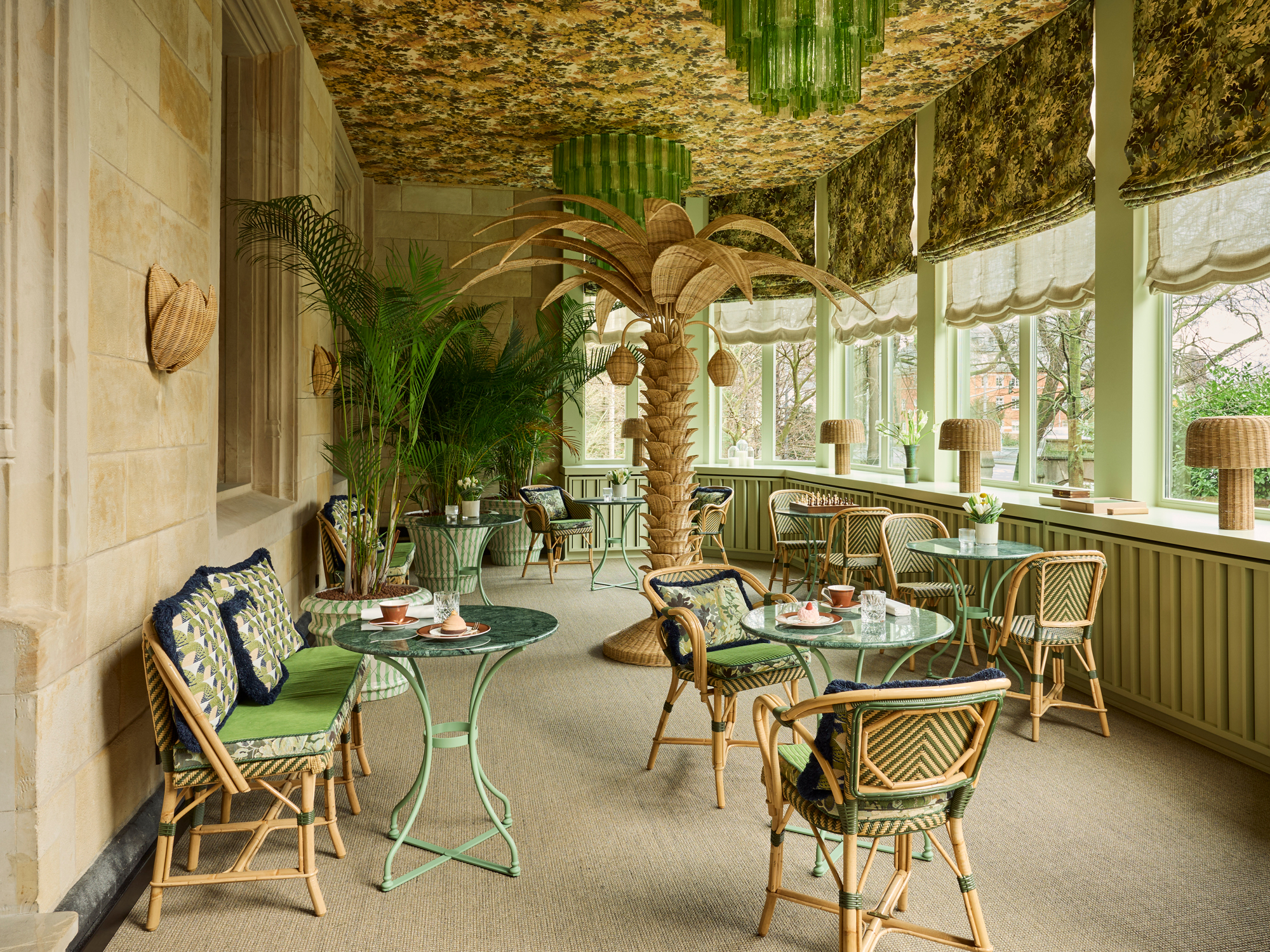Brightly decorated winter garden featuring rattan furniture, green accents, and a large palm centerpiece.